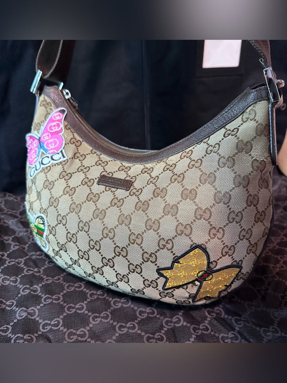 This is a Gucci GG canvas half-moon hobo bag featuring decorative patches.